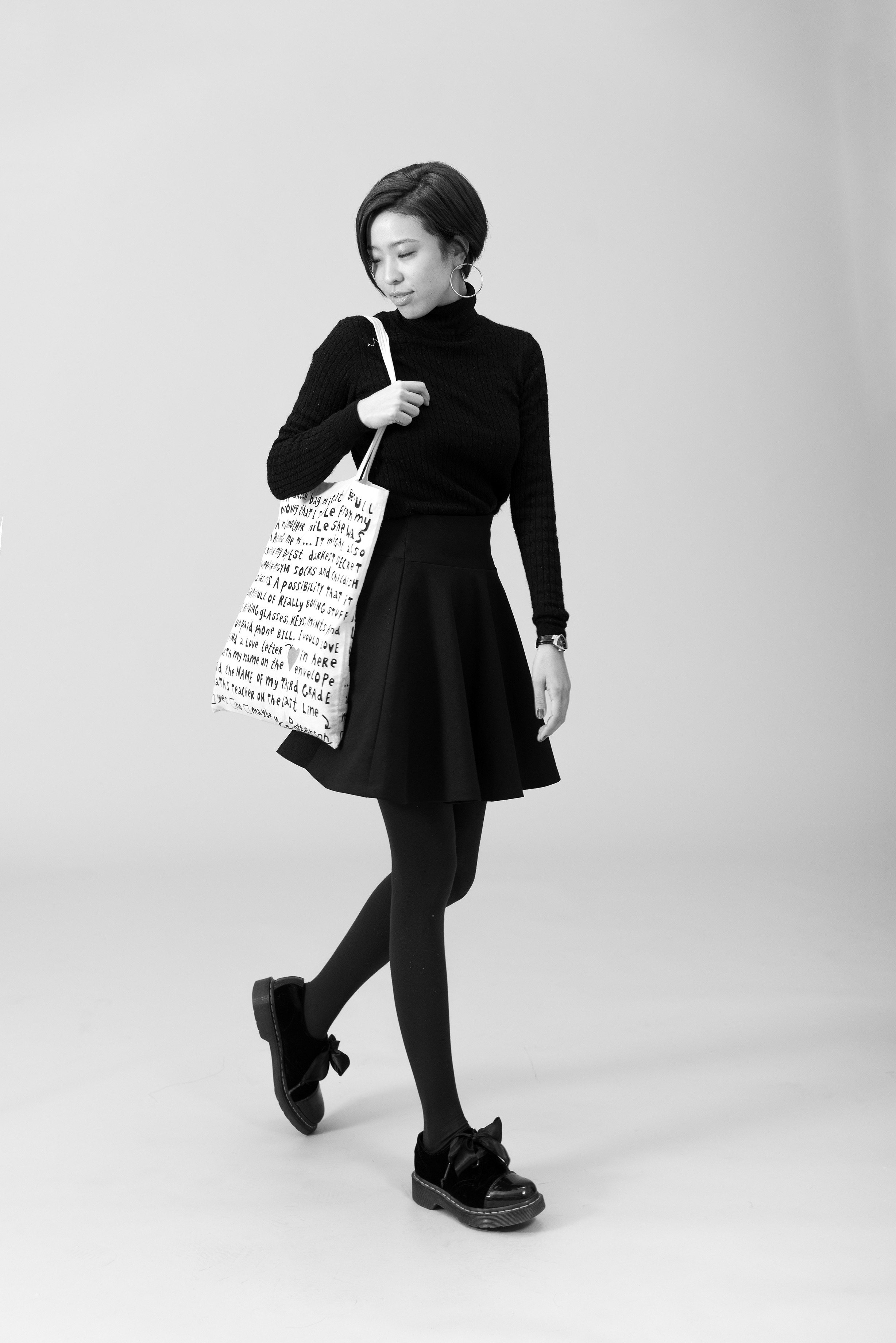 たくさん英語が書いてあるトートバックを肩から下げた、黒ずくめの女（実寸）